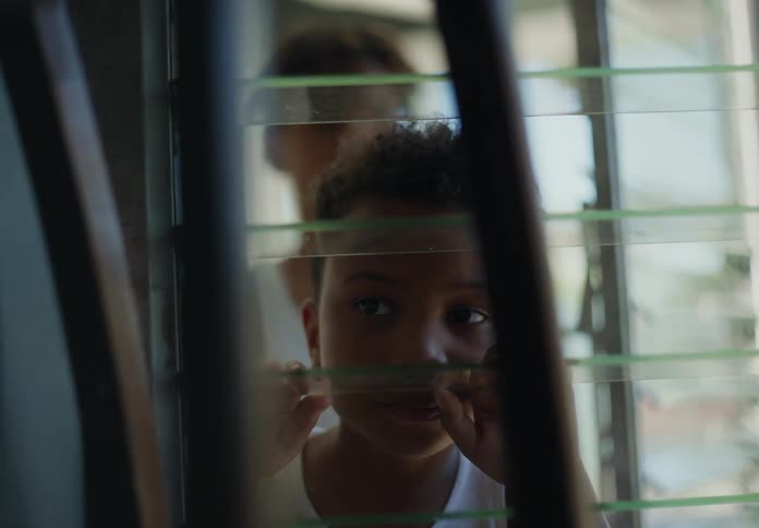 A young boy walks up to a window and looks out of it with curiosity