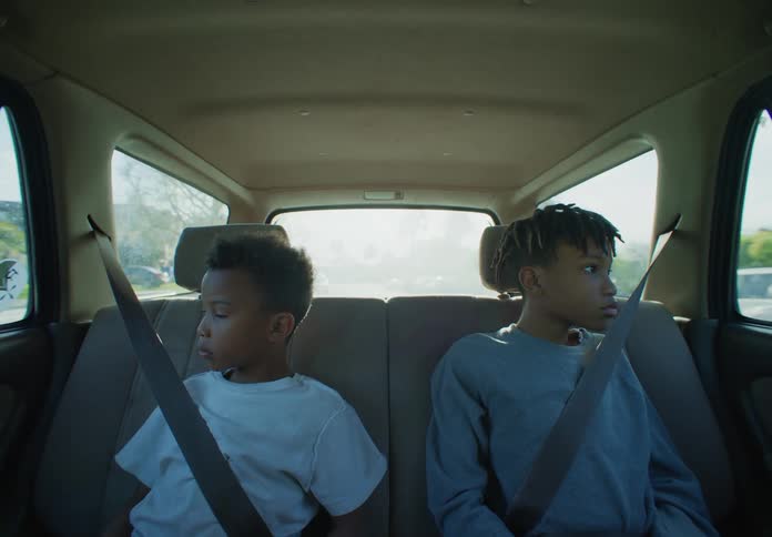 Two boys are sitting in the back seat of a traveling automobile with their seat belts on as they look out the windows