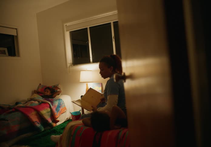 A mother reading to her sons in their bedroom while they lay in their beds
