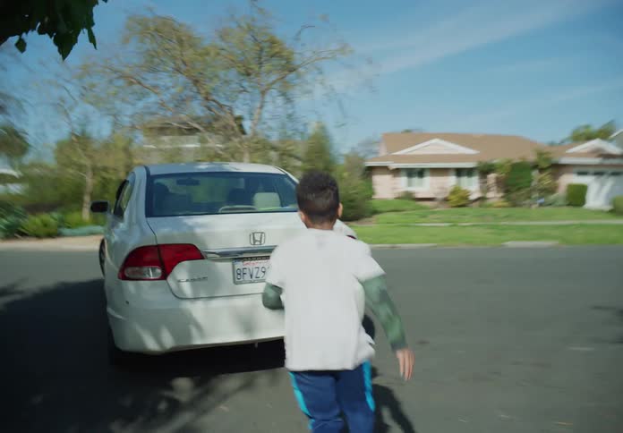 A young boy is chasing and waving at a car driving away on a neighborhood street