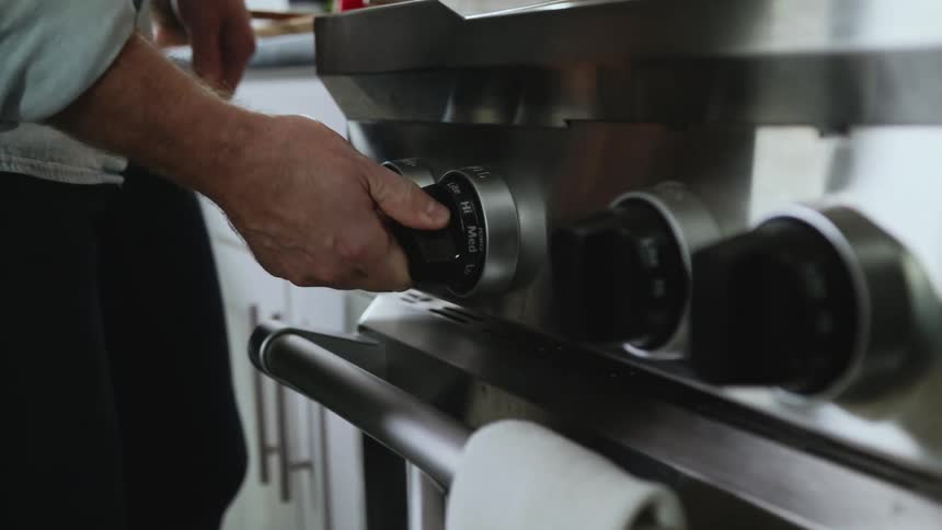 A close up of a persons hand turning a dial on the stove