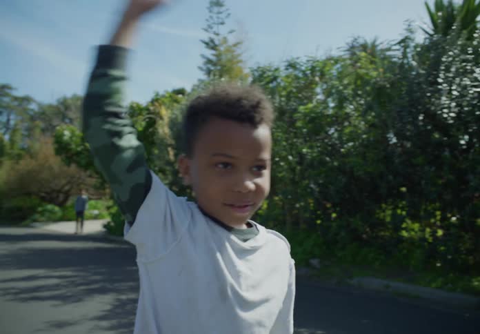 A young boy is running on a neighborhood street and he stops to wave as another boy is running in the distance