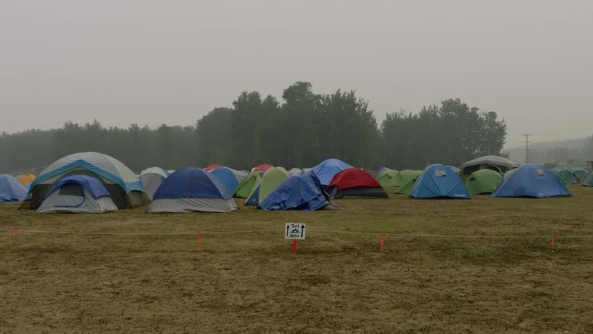 A bunch of colored tents are grouped together in a grassy field cordoned off with rope