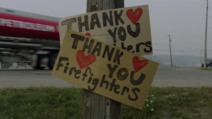 Handmade signs thanking firefighters are posted on a telephone pole near a busy road