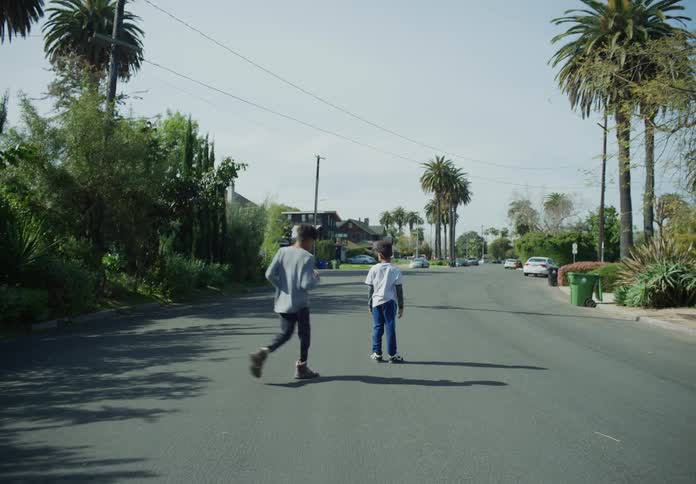 A boy chases a white car down the street and another boy joins him in the road