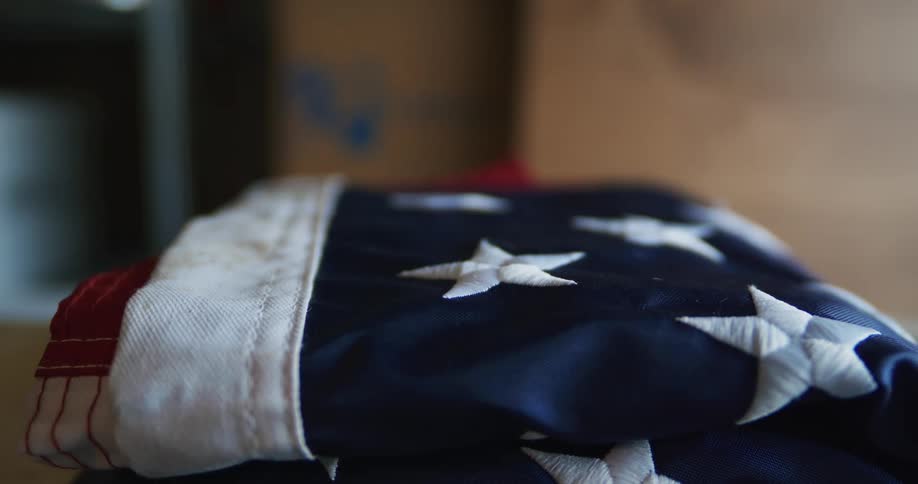 Close up of the hands of a person placing a folded american flag over a table