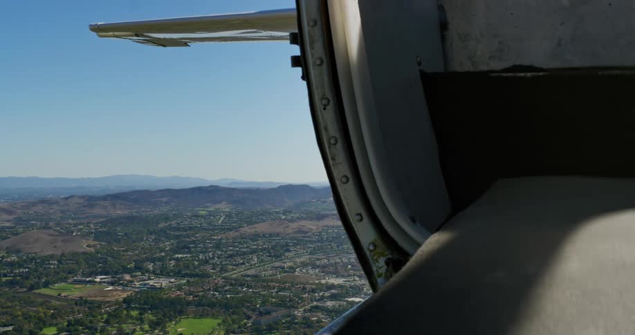 Aircraft moves over town bordered by hills and foggy mountains