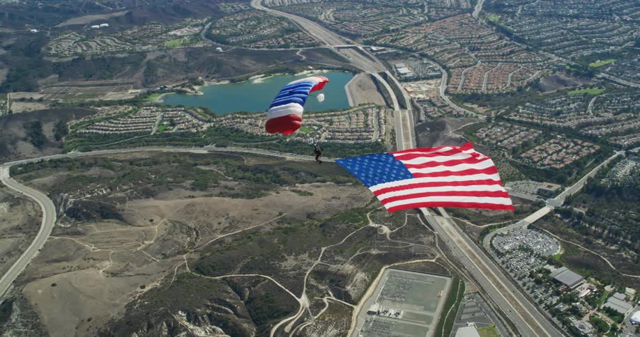 A man trailing an american flag parachutes over a suburban area