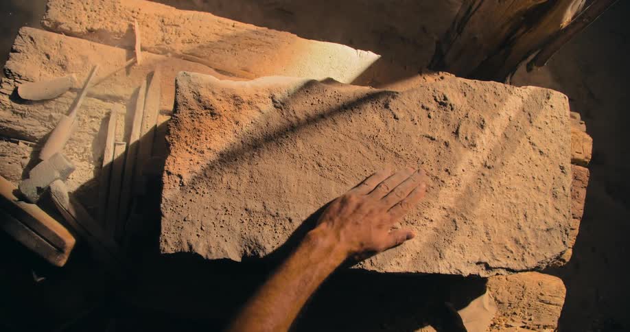 A person is brushing away dirt and dust from a flat rock at an archeological site