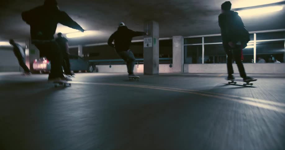 A small group of teenage boys are riding their skateboards through a parking garage at night