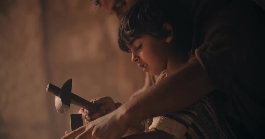 A father teaches his son how to sculpt rock using a hammer and a chisel