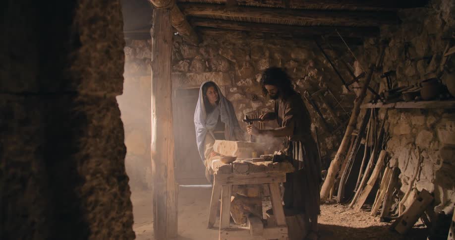 A man uses a chisel and hammer on a large stone as a woman watches