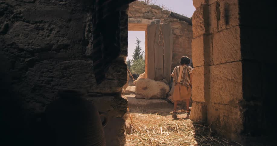 Boy from traditional biblical times running out of the home to meet his mother sitting in the yard