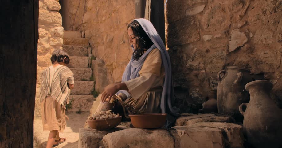 Mother from traditional biblical times working on the yard kisses her son in the forehead