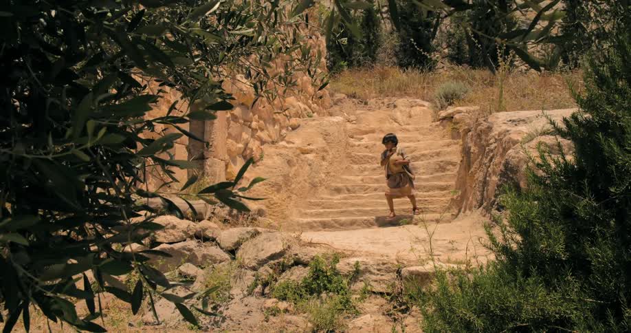 A boy walks down outdoor steps while carrying a jug during the day