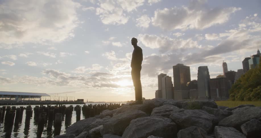 A man is standing on rocks by the water