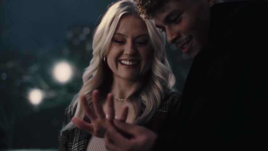 A man and woman getting engaged putting the ring on the womans finger hugging and smiling