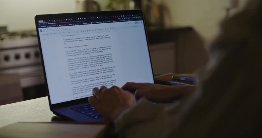 A person is sitting at a kitchen counter and typing on a laptop