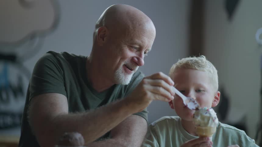 A man uses a spoon to feed a boy chocolate ice cream before using the spoon to take a scoop of the boys vanilla ice cream
