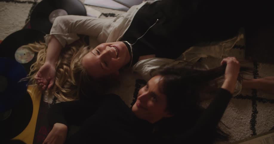 Two young friends lay next to each other over the carpet on the floor of a room listening to music