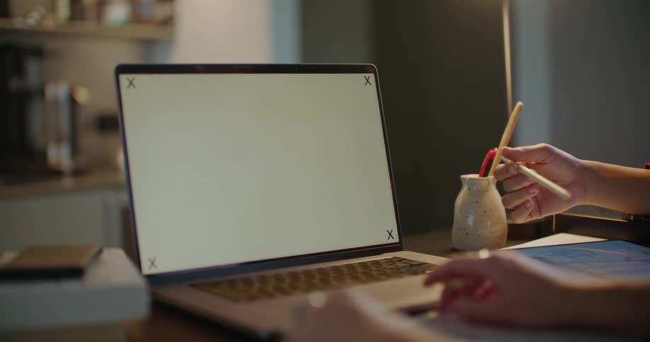 A person holds a pen and types on a laptop keyboard