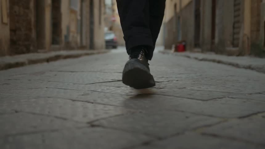 A persons feet as they walk on a stone road between buildings