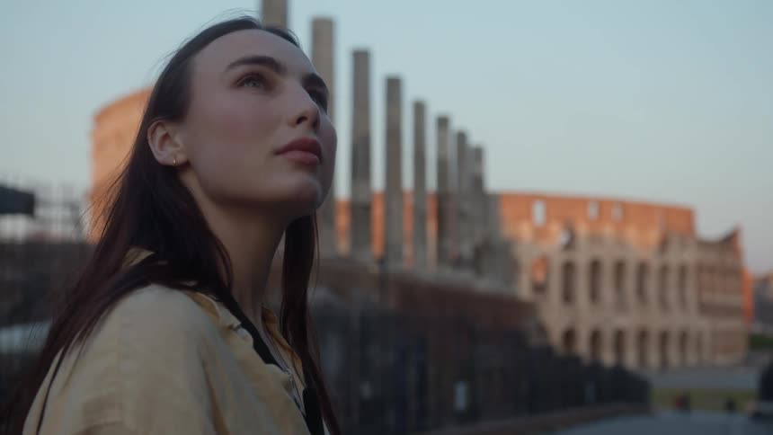 Close up of the face of a woman turning around to see the colosseum in the morning