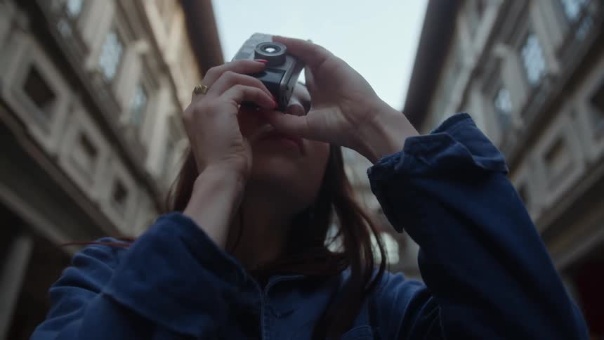 A woman takes out her camera to take a photo of a building