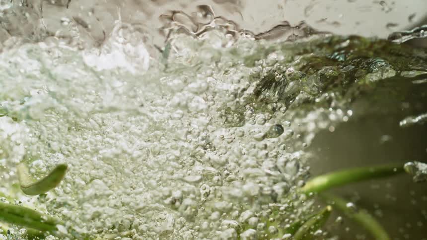 Green beans being dropped into water creating water splashing up and droplets
