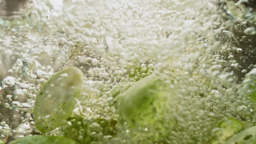 Halved brussel sprouts are dropped into water in slow motion creating a splash and bubbles
