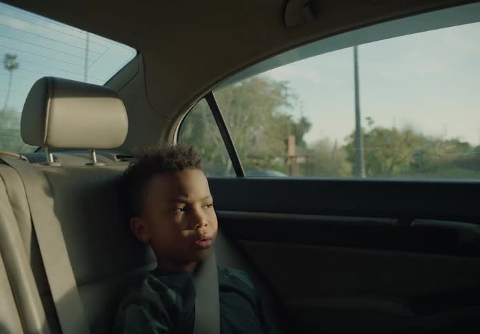 A boy siting in the back seat of a moving car stares straight ahead