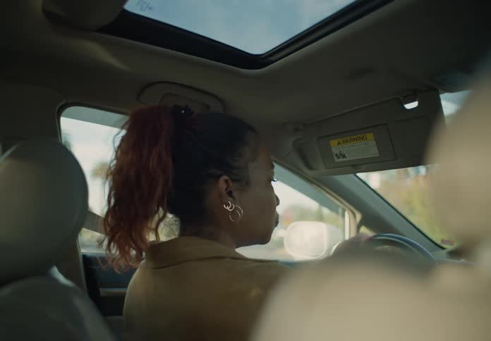 A woman is sitting in the driver seat of an automobile and looking around as she drives through a neighborhood