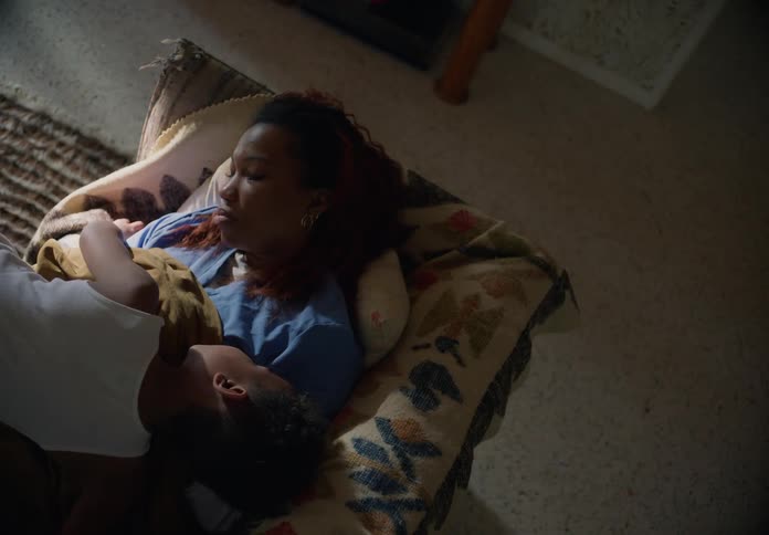 A woman sleeping on her couch when her son comes over and pokes at her lays on her and puts his hand on her forehead