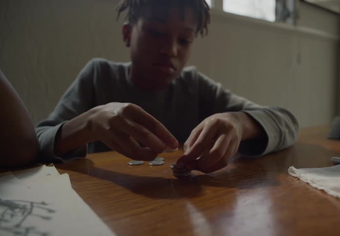 Young bored boy entertaining himself piling coins one over the other over a table