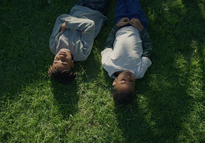 Brothers laying on their backs on the grass facing up with the sun on their faces