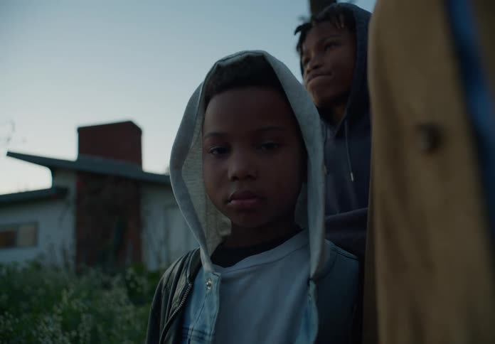 Two boys with dreadlocks and hoodies face the camera with eye contact outdoors at dusk
