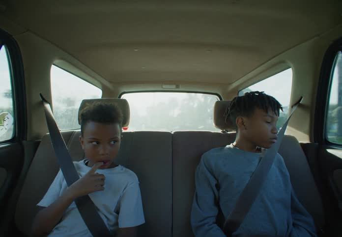 Two boys are sitting in the back seat of a traveling automobile with their seat belts on as they look out the windows
