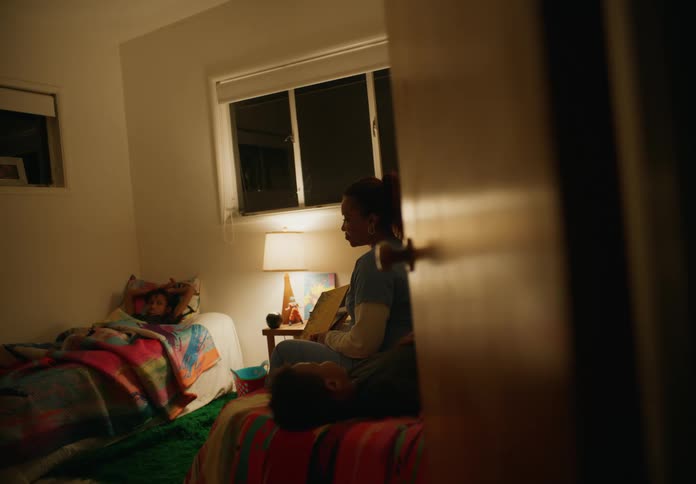 A mother sitting on her sons bed across from another son looking adn talking to them