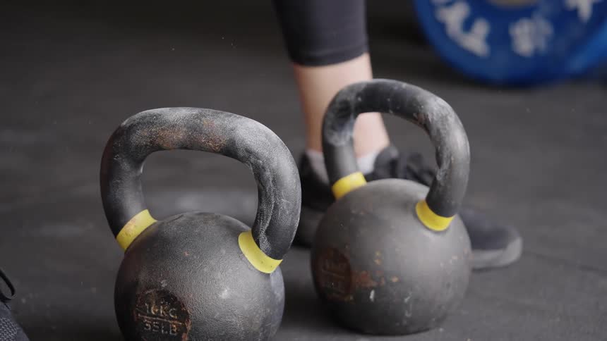 A woman picks up two kettlebells while working out