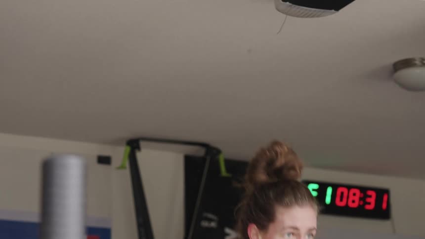 A woman is lifting large dumbbells above her head