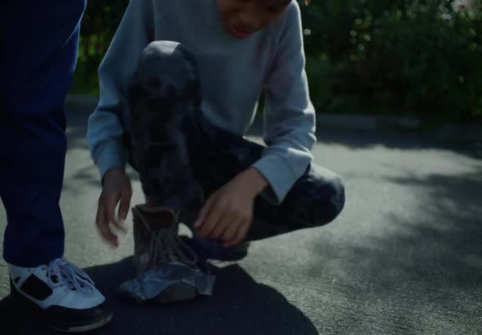 Young boy standing next to his brother on the backyard kneels to tie the laces on his shoes