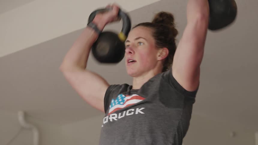 Close up of the face and arms of a strong muscular woman lifting weights over her head