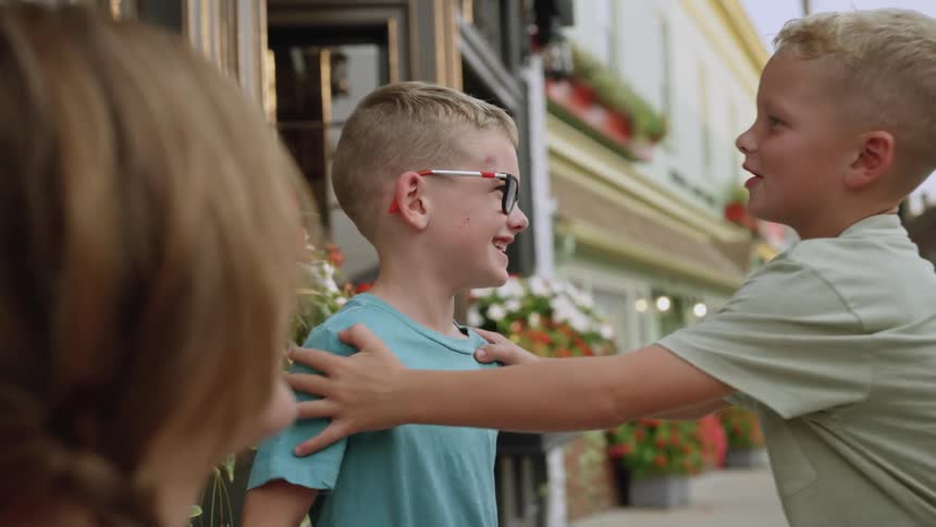 Two happy brothers standing on the sidewalk next to potted flowers on the facade of a building