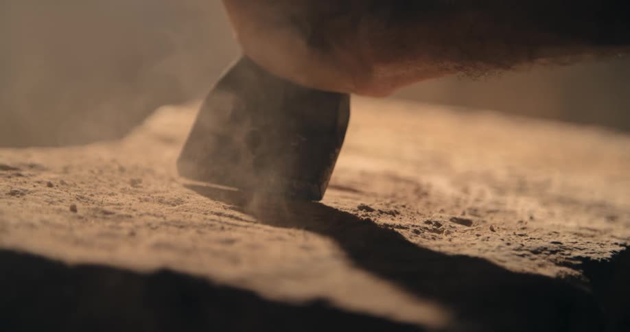 A hand holds a chisel onto stone