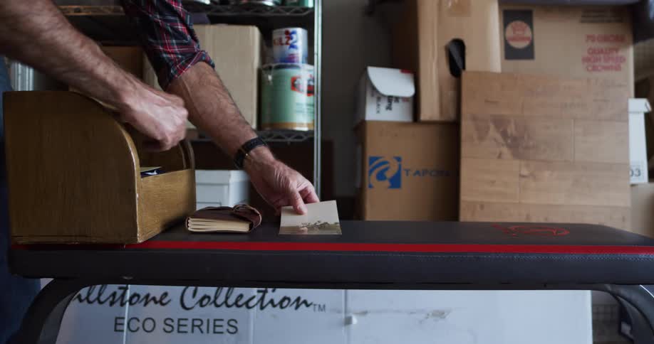 Man in a garage opens up a wooden box and pulls several keepsake items out and sets them on a table