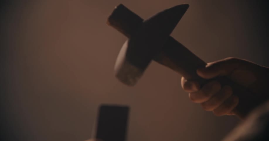 Craftsman hammers on end of metal bar while working in workshop