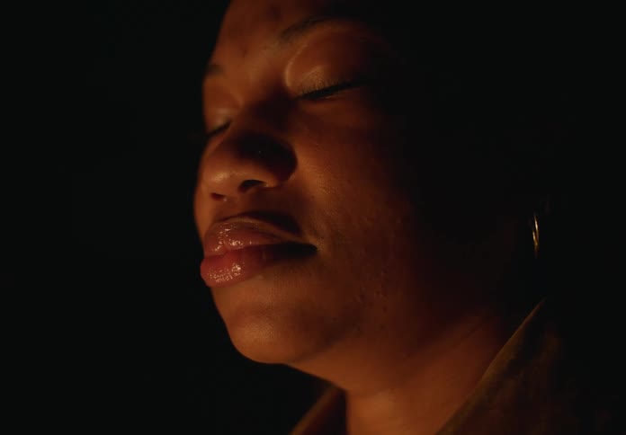 A close up of a black womans face is shown closing her eyes then looking at the camera and swallowing