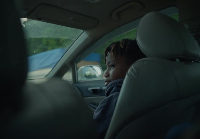 A young boy is sitting in the passenger seat of an automobile looking around as they travel through the suburbs
