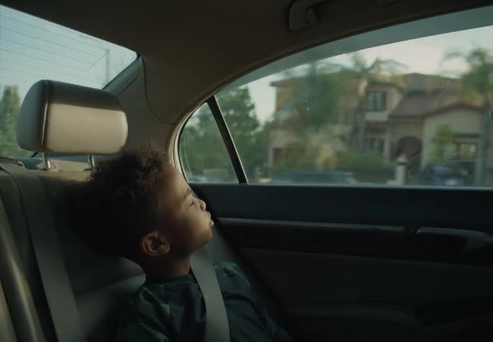A boy riding in the back of a car with his seat belt on looking around