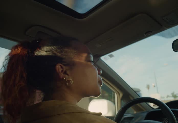 A woman is sitting in the driver seat of an automobile and looking around as she drives through the suburbs